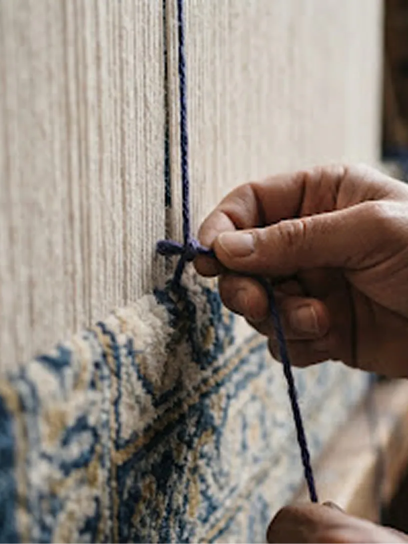 An artisan's hands carefully tying knots on a traditional rug loom